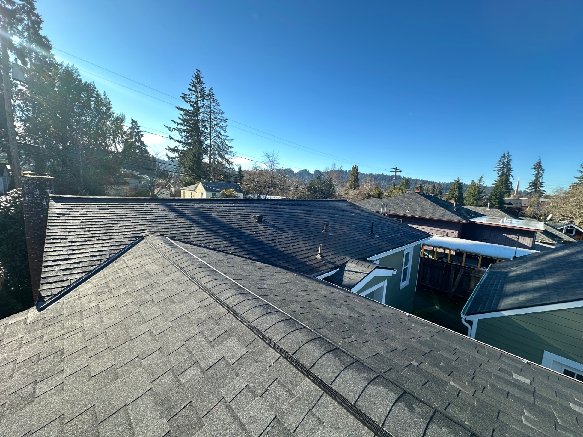 Ground-level view of charcoal shingle roof with mountain and town backdrop — Newport, OR
